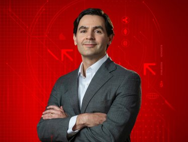 Portrait of Brad Chandler posing with crossed arms against a red graphic background featuring cryptocurrency logos and blockchain graphics.