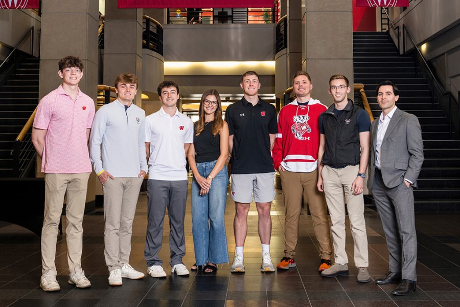 A group of seven students and instructor Brad Chandler pose together in a row inside a campus atrium.