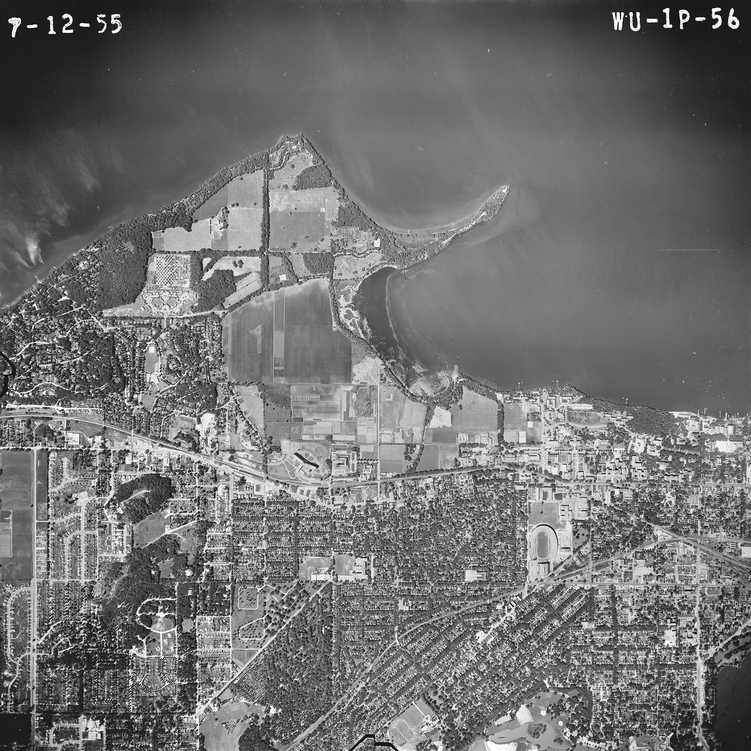 A black-and-white aerial photograph of the UW–Madison campus shoreline along Lake Mendota, showing Picnic Point, University Bay, and surrounding agricultural fields and residential areas.