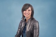 Portrait of Lisa Yaszek smiling in a metallic jacket against a light blue backdrop.