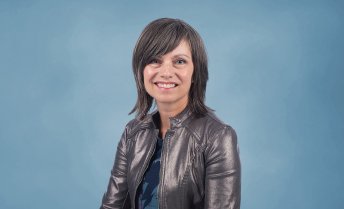 Portrait of Lisa Yaszek smiling in a metallic jacket against a light blue backdrop.