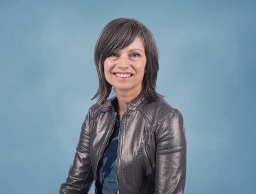 Portrait of Lisa Yaszek smiling in a metallic jacket against a light blue backdrop.