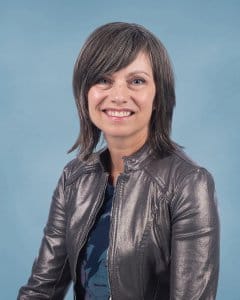 Portrait of Lisa Yaszek smiling in a metallic jacket against a light blue backdrop.