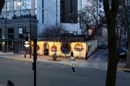 An elevated street view at dusk of the illuminated exterior facade and courtyard wall of Porta Bella Italian Restaurant along a city sidewalk.