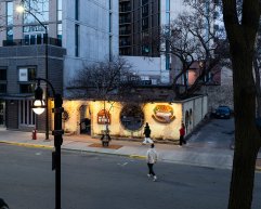 An elevated street view at dusk of the illuminated exterior facade and courtyard wall of Porta Bella Italian Restaurant along a city sidewalk.