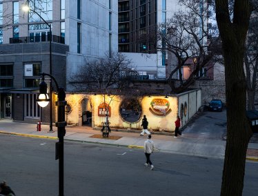 An elevated street view at dusk of the illuminated exterior facade and courtyard wall of Porta Bella Italian Restaurant along a city sidewalk.