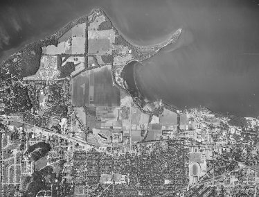 A black-and-white aerial photograph of the UW–Madison campus shoreline along Lake Mendota, showing Picnic Point, University Bay, and surrounding agricultural fields and residential areas.