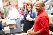 Eric Wilcots, smiling and wearing a red Wisconsin shirt, holds a cup of ice cream handed to him by a volunteer at an employee ice cream social.