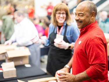 Eric Wilcots, smiling and wearing a red Wisconsin shirt, holds a cup of ice cream handed to him by a volunteer at an employee ice cream social.