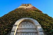 A low-angle view looking up at the ivy-covered Memorial Carillon tower and its inscribed stone entryway against a clear blue sky.