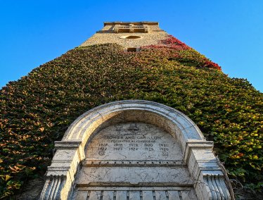 A low-angle view looking up at the ivy-covered Memorial Carillon tower and its inscribed stone entryway against a clear blue sky.
