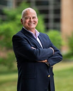 Portrait of Paul Hutson standing outdoors with arms crossed, wearing a navy blazer and a light purple dress shirt.