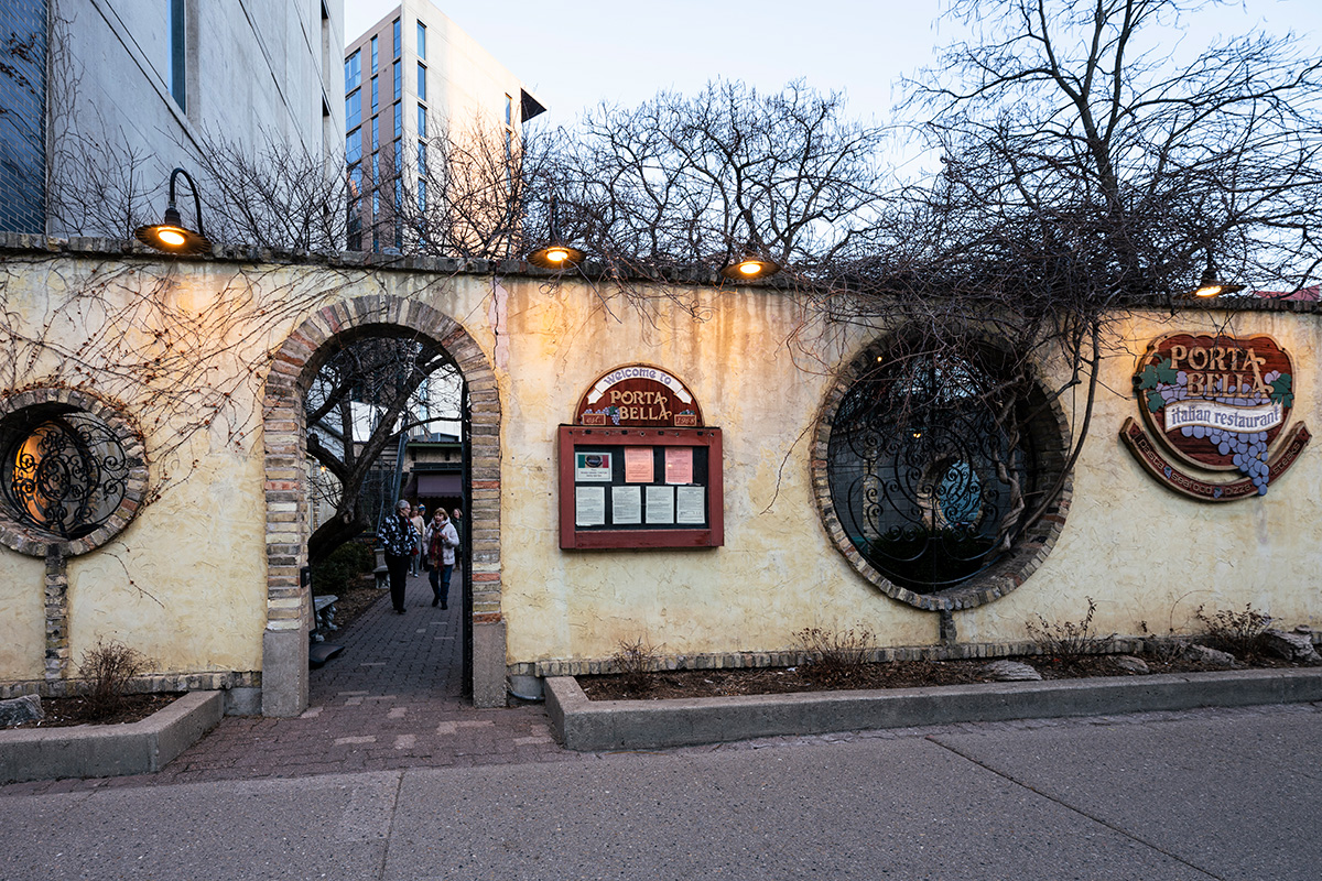 The warm, illuminated stucco exterior wall and brick archway entrance of Porta Bella Italian Restaurant at dusk.